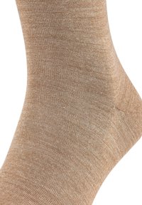 Calcetín beige con un acabado de punto suave y texturizado, de ajuste ceñido, diseñado para ofrecer comodidad y estilo, destacando sutiles variaciones de color.