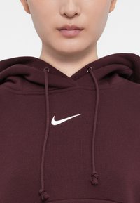 Hoodie bordeaux com um logo Nike branco no peito, apresentando um capuz com cordão e um tecido texturizado para conforto.