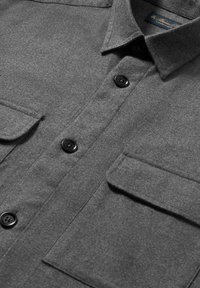 Camicia grigia con bottoni realizzata in tessuto testurizzato, dotata di colletto a punta, due tasche sul petto con pattina e bottoni neri.
