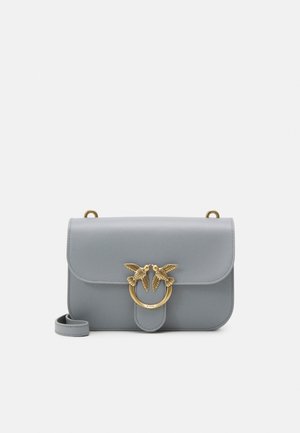 Borsa a tracolla in pelle grigia con fibbia ad anello dorata che presenta due uccelli e una lunga tracolla regolabile posizionata su sfondo bianco.