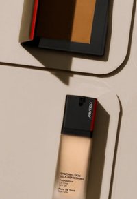 Botella de base de maquillaje Shiseido Synchro Skin Self-Refreshing; cristal transparente, tapa negra y roja, libre de aceite, SPF 30; compacto con polvo marrón.