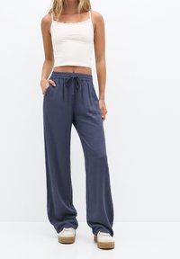Losse, donkerblauwe linnenbroeken met een elastische tailleband en trekkoord, voorzien van zijzakken, gecombineerd met een witte geribbelde crop top.