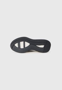 Shoe sole with a wave pattern, featuring black rubber with grooves for traction and cream-colored accents on the side.