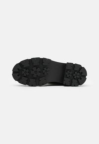 Semelle en caoutchouc noir avec une surface texturée, présentant des motifs de semelle circulaires et floraux bien marqués pour une adhérence et une traction accrues.