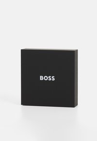 Svart rektangulær boks med en glatt tekstur og en hvit "BOSS"-logo foran. Enkelt design med skarpe hjørner og uten ekstra mønstre.
