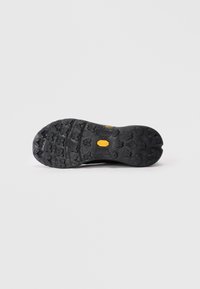 Juodas batų padas su tekstūruotu, daugiakampiu guminio rašto dizainu ir geltonu "Vibram" logotipu centre, ant vientiso balto fono.