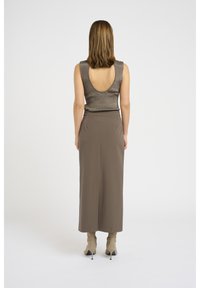 Top sans manches en métal marron avec un dos bas ; associé à une jupe longue taille haute de couleur taupe unie. Accessoirisé avec des bottines beige.
