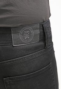 Černé džínové kalhoty z denimu s hladkou texturou; mají koženou nášivku na zadním pásu vyraženou s logem značky a detaily.