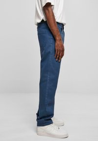 Pantalons en coton bleu avec une coupe droite, poches latérales et une texture lisse. Assortis à des baskets blanches, vus de côté.