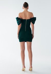 Zielona dopasowana sukienka z odkrytymi ramionami i bufkami przy rękawach, z marszczeniami i zamkiem błyskawicznym z tyłu. Beżowe sandały na wysokim obcasie z paskami.