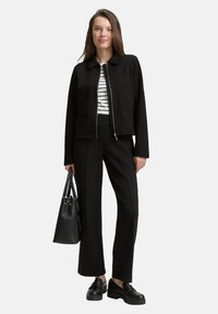 Black cropped jacket with a collar, striped shirt underneath, tailored black pants, and black platform shoes. Holding a black handbag.