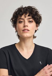 Svart V-ringad t-shirt gjord av mjukt tyg, med en liten vit logotypdetalj på vänster bröst, korta ärmar och en klassisk passform.