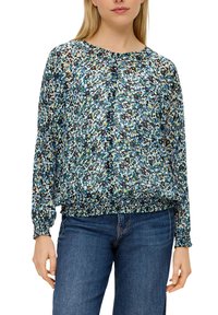 Leichte Bluse mit langen Ärmeln im mehrfarbigen abstrakten Muster, mit rundem Ausschnitt und gerafftem Saum. Kombiniert mit blauen Jeans.