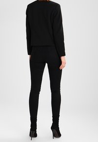 Czarna dopasowana kurtka z długimi rękawami, teksturowany materiał, skrócony fason. Połączona z czarnymi wąskimi dżinsami i butami na wysokim obcasie.