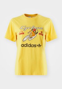 Yellow cotton t-shirt featuring a bicycle graphic, "Cyclone" text, and the Adidas logo prominently displayed at the bottom. Short sleeves.