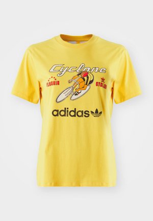 Dzeltena kokvilnas T-kreklu ar velosipēda grafiku, tekstu "Cyclone" un Adidas logo izcelti apakšā. Īsas piedurknes.