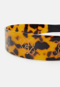 Bandeau en écaille de tortue avec une finition brillante et des motifs floraux en relief dorés. Design rond avec une texture lisse.