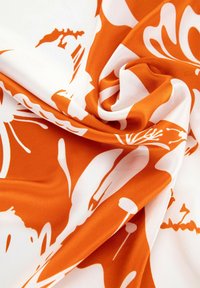 Květinová látka v oranžových a bílých barvách, s hladkou texturou. Design zahrnuje velké květiny a abstraktní tvary v plynulém uspořádání.