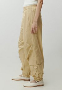 Beige lichtgewicht cargobroek met een elastische tailleband, zijzakken en verstelbare enkelboorden, met een gladde, glanzende textuur.