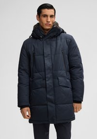 Donkerblauwe gewatteerde jas met een capuchon, voorzien van rits- en klepzakken, en een gestructureerde voering. De stof lijkt glad en waterafstotend.