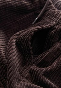 Mörkbrun, ribbad kordflor tyg med en mjuk textur som visar djupa fåror och en slät innerskikt, vikt för att avslöja djup.