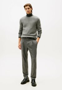 Suéter de punto gris con cuello alto simulado, combinado con pantalones grises texturizados, ambos con un diseño sutil. Unos zapatos de cuero negro completan el conjunto.