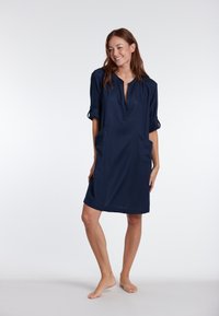 Abito blu navy con scollatura a V e maniche arrotolate, dotato di due tasche frontali e design ampio fino al ginocchio. Tessuto dalla texture liscia.