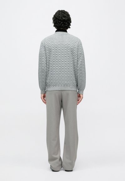 Camisola cinzenta com padrão e gola preta, combinada com calças cinza claras, vista de trás. Design texturizado e corte descontraído.