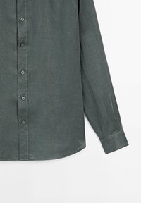 Chemise à manches longues gris foncé avec boutons et poignets standards, présentée sur fond blanc, montrant le devant et une manche.