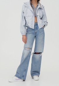 Ljusblå kort jacka med huva och framfickor, kombinerad med slitna jeans med vida ben. Vita sneakers med lila accenter.