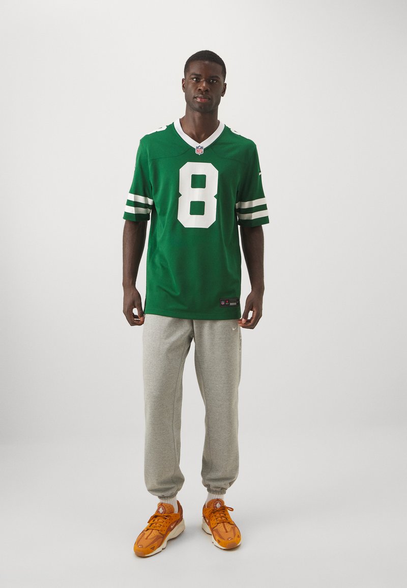 Zielony T-shirt NFL z białym numerem 8, krótkie rękawy i paski, w połączeniu z szarymi spodniami dresowymi i pomarańczowymi sneakersami.