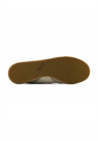 Sohle eines Schuhs mit einer strukturierten Gumm Oberfläche in Hellbraun mit kreisförmigen Mustern, und einem flexiblen, beigen Obermaterial.