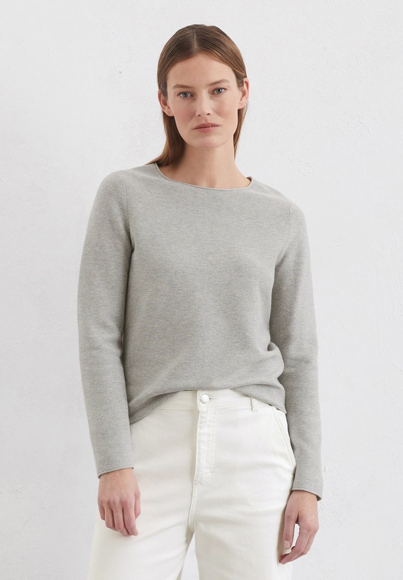 Lichtgrijze trui met lange mouwen en een ronde hals, gemaakt van een zachte stof, gecombineerd met witte jeans in een relaxte pasvorm.