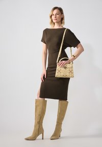 Ruskea ribbineuloksinen mekko, jossa on lyhyet hihat ja sivuhalkio, yhdistetty polven korkeisiin vaaleanbeigeihin mokkanahkasaappaisiin ja kuvioituun keltaiseen käsilaukkuun.