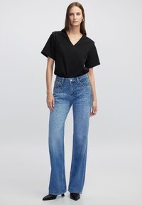 T-shirt nero con scollo a V e applicazioni di borchie sulle spalle, abbinato a jeans a gamba larga di un blu chiaro con decorazioni a pois e un taglio classico.