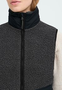 Grauer Fleece-Weste mit hohem Kragen, Reißverschluss und schwarzen Akzenten. Strukturierten Oberfläche, weichem Material und taillierter Passform.