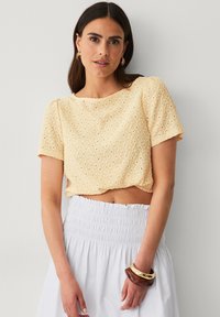 Gul cropped top med en struktureret eyelet-design, korte ærmer og en rund halsudskæring, parret med en hvid, smocked talje nederdel.