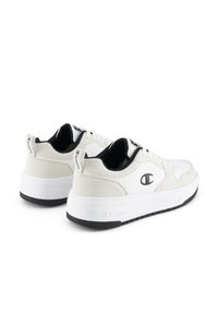 Białe sneakersy z teksturowaną górą z zamszu i skóry, czarnymi akcentami, sznurowadłami oraz logo, z grubą gumową podeszwą i charakterystycznymi elementami na pięcie.
