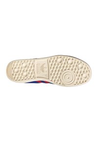 Shoe sole in beige rubber with a textured pattern. Features include circular and oval indentations, with branding in the center.