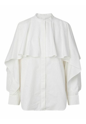 Hvit bluse med lange ermer, høy krage og lagvis kappeaktig stoff som draperer over skuldrene og overarmene, knappet ved halsen.