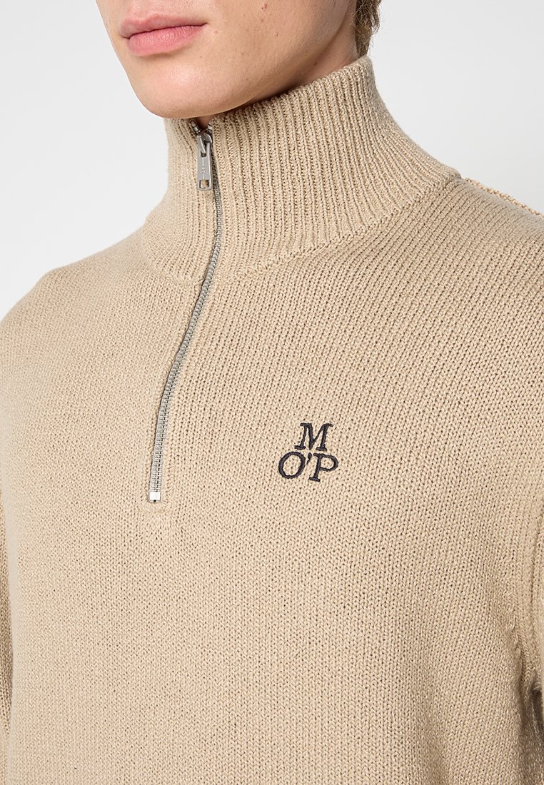 Beige gebreide trui met hoge kraag, zilveren rits en geborduurd "MOP" logo op de linkerborst. Textuurstof met een casual pasvorm.