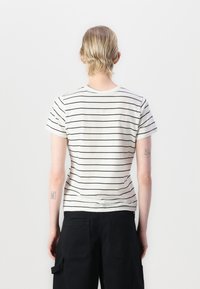 T-shirt bianco con strisce orizzontali nere, maniche corte, collo rotondo e forma aderente. Indossato con pantaloni cargo neri.
