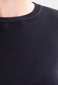 Pull bleu marine avec une texture lisse, doté d'un col ras du cou classique et de bords côtelés. Le matériau semble doux et chaud.