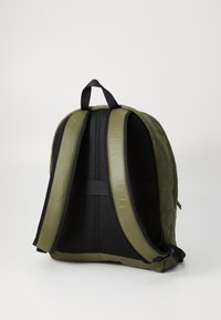 Sac à dos matelassé vert avec des bretelles noires rembourrées et un panneau arrière en mesh. Il possède une poignée supérieure et une forme arrondie élégante.