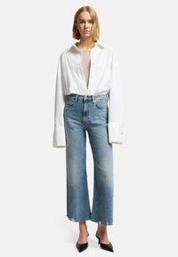 Camicia bianca con bottoni e ampi polsini, abbinata a jeans azzurri a vita alta con orlo sfilacciato. Tacchi neri a punta.