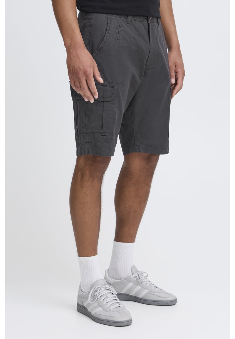 Harmaat cargo-shorts, jotka on valmistettu puuvillasta, sivutaskuilla, ommelluilla yksityiskohdilla ja rentolla leikkauksella, yhdistettynä harmaisiin lenkkareihin ja valkoisiin sukkiin.