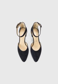 Melni zamšādas augstpapēžu apavi ar smailiem purngaliem, potītes siksniņu un gaišām zolēm, raksturīgi ar gludu tekstūru un minimālisma dizainu.