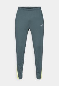 Tmavě modré sportovní kalhoty s elastickým pasem, zúženými nohavicemi a jasně žlutými akcenty po stranách. Na přední straně se nachází bílé logo.