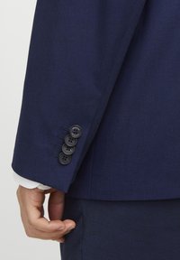 Manga de chaqueta de traje azul marino con cuatro botones negros y una textura sutil. Parte inferior lisa con un acabado suave.
