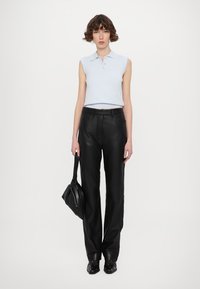 Polo sans manches bleu clair avec un col, associé à un pantalon en cuir noir taille haute ; tenant un sac à main noir ; chaussures noires.